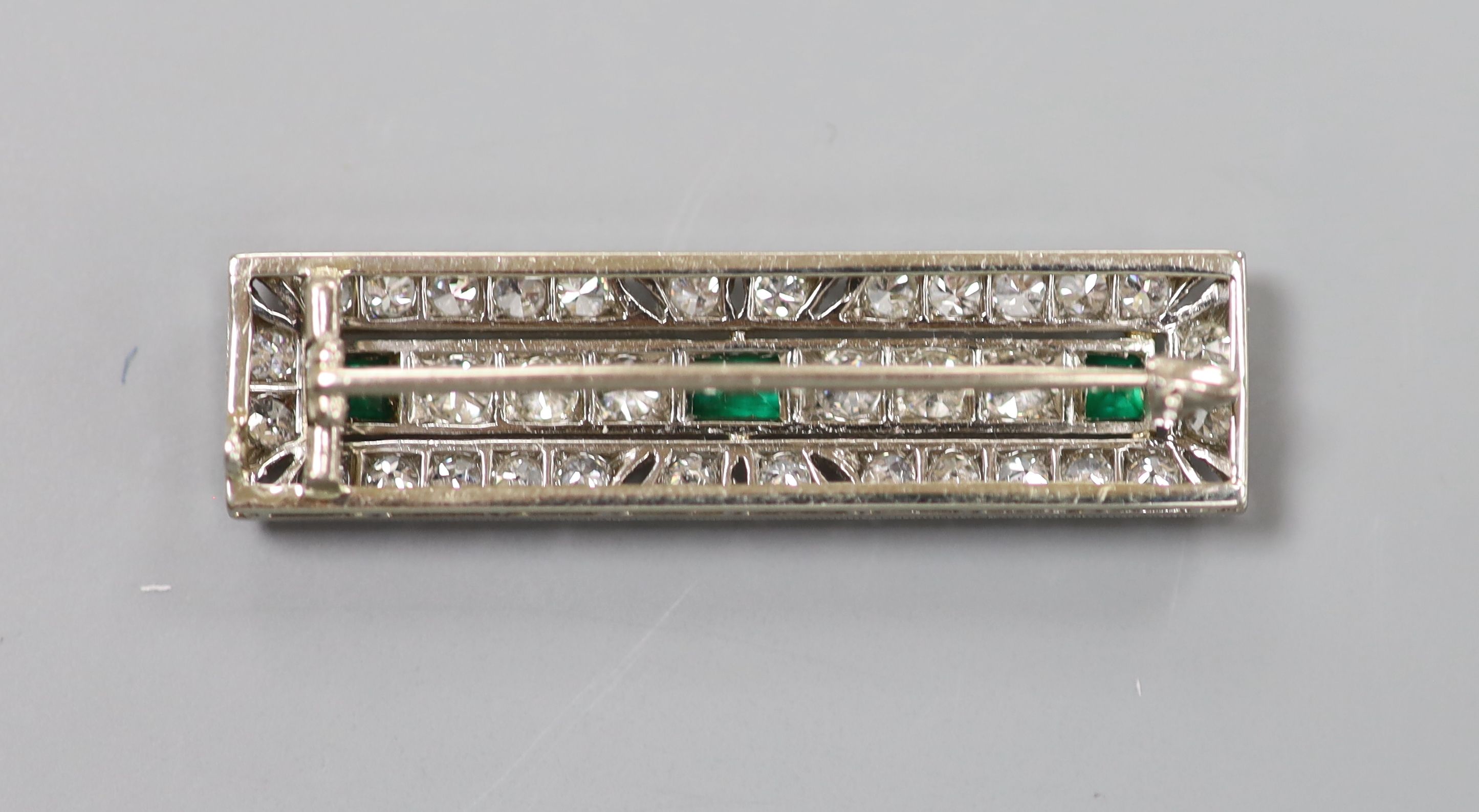 An Art Deco pierced 18ct and plat, emerald and diamond millegrain set rectangular brooch